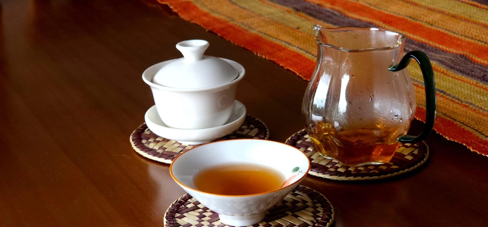 Chá servido em gaiwan, xícara e jarra de vidro sobre mesa de madeira